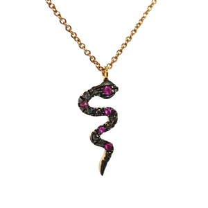 Puede incluir: Un collar de cadena dorada con un colgante de serpiente negra adornado con pequeñas piedras preciosas rosas.