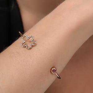 May include: A gold bangle bracelet with a flower-shaped design set with small diamonds. The bracelet has a small purple gemstone on the clasp.