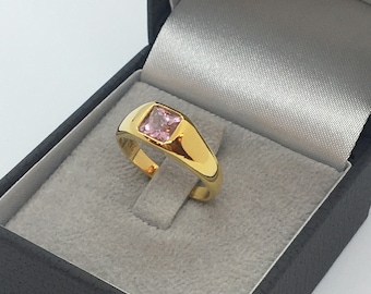 May include: A gold ring with a square pink gemstone set in the center. The ring is in a black velvet ring box.