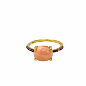 Puede incluir: Un anillo de oro con una piedra ovalada rosa y una banda de pequeñas piedras rosas y transparentes.