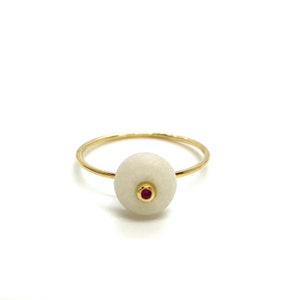 May include: A gold ring with a white stone and a small red gemstone in the center.