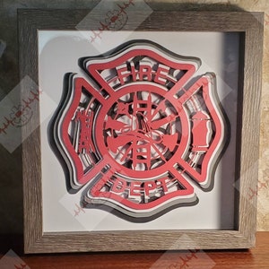 May include: A red, gray, and white layered paper fire department emblem with the words "FIRE DEPT" in a circle. The emblem is framed in a brown wood frame.