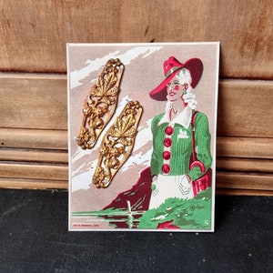 May include: Two gold-toned metal buttons with a floral design. The buttons are displayed on a card with a woman wearing a green sweater and a red hat.