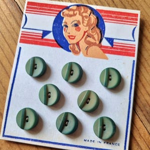May include: A vintage card of eight green buttons with a diagonal groove design. The card features a retro illustration of a woman in a blue circle, with red and white stripes. The text "MADE IN FRANCE" is printed at the bottom.