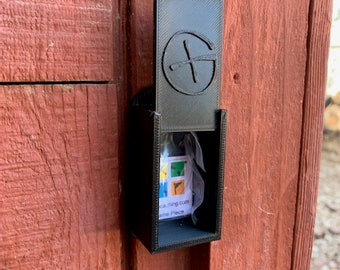 May include: A black plastic box with a clear plastic window, containing a small, folded piece of paper with a compass and the text "geocaching.com" and "Summer Place". The box is attached to a wooden surface with a black plastic bracket. The box has a small, black plastic lid with a compass symbol.