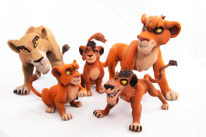May include: Five handmade clay lion figurines, including a mother lion, a father lion, and three cubs. The lions are all orange and brown with black eyes and noses. The mother lion is standing on all fours, while the father lion is standing on his hind legs. The cubs are sitting on their haunches.