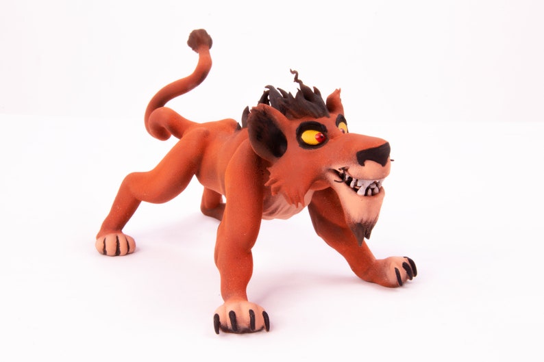 May include: A red and black lion figurine with a menacing expression. The lion has sharp teeth and claws, and its eyes are bright yellow. The figurine is made of a soft, pliable material, possibly clay or polymer clay.