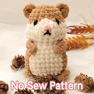 Puede incluir: Un hámster de ganchillo hecho a mano en tonos marrón y crema, con una nariz rosa y ojos negros. El texto "No Sew Pattern" se muestra en la parte inferior de la imagen. El hámster está rodeado de piñas.