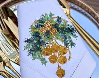 May include: White linen napkin with an embroidered design of a green pine bough with gold bells and pine cones.