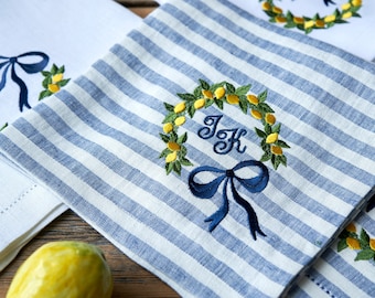 May include: Set of four kitchen towels with embroidered lemon wreaths. Two towels are white with blue embroidery and two towels are blue and white striped with blue embroidery. One of the striped towels has the initials "J.K." embroidered in the center of the wreath.