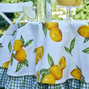 Pu&ograve; includere: Tovaglia bianca con un bordo a quadri verdi e bianchi. La tovaglia presenta una stampa di limone con limoni gialli e foglie verdi.