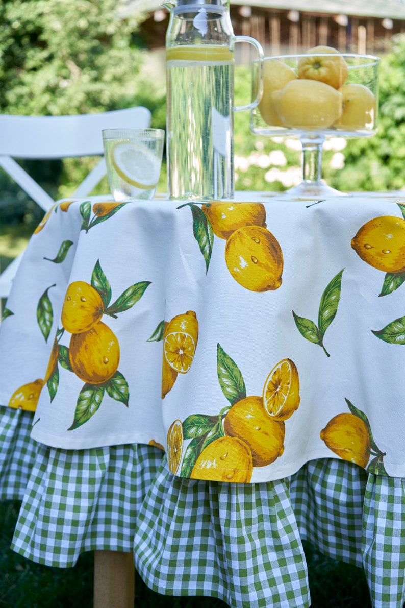 Pu&ograve; includere: Tovaglia bianca con un bordo a quadri verdi e bianchi. La tovaglia presenta una stampa di limone con limoni gialli e foglie verdi.
