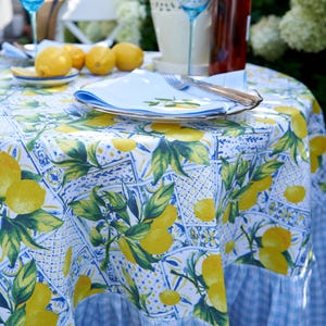 May include: A blue and white tablecloth with a lemon print and a gingham border. The tablecloth is set with a white plate, a blue napkin, and silverware.