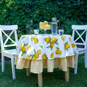 Pu&ograve; includere: Tavolo bianco con una tovaglia a quadri gialla e bianca con stampa di limoni. Due sedie bianche sono posizionate su entrambi i lati del tavolo. Una caraffa di vetro d'acqua e due bicchieri sono sul tavolo.