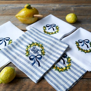 May include: Four embroidered kitchen towels with a lemon wreath design. Two towels are white with a blue bow and a lemon wreath. Two towels are blue and white striped with a blue bow and a lemon wreath. One towel has the initials "J & K" in the center of the wreath.
