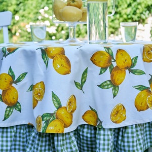 Pu&ograve; includere: Tovaglia rotonda bianca con un bordo a quadri verde e bianco. La tovaglia presenta una stampa di limone con limoni gialli e foglie verdi.