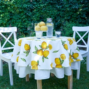 Pu&ograve; includere: Tavolo bianco con una tovaglia a stampa di limone apparecchiato per due con due sedie bianche. Un'ampolla di vetro di limonata e un bicchiere di limonata sono sul tavolo.