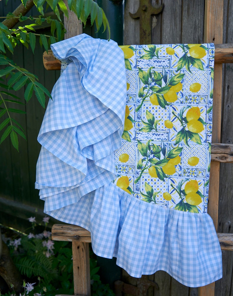 May include: A blue and white gingham tablecloth with a ruffled edge. The tablecloth features a lemon print with green leaves and a blue and white tile pattern.