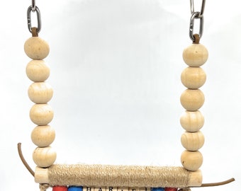 May include: A wooden bird swing with the name "HARLEY" spelled out in letter beads. The swing features natural wood beads, a jute-wrapped perch, and red and blue accent beads. It hangs from a metal chain and a carabiner clip.