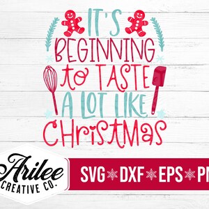 Può includere: Testo rosso e blu su uno sfondo di legno bianco che dice "It's beginning to taste a lot like Christmas".  Ci sono due omini di pan di zenzero e una frusta e una spatola nel design.  Il testo "Arillee Creative Co. SVG DXF EPS PNG" è nella parte inferiore dell'immagine.