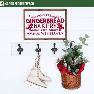 Może przedstawiać: Biała ściana z drewnianym znakiem z napisem "ALWAYS FRESH GINGERBREAD BAKERY" na czerwono. Poniżej znaku znajduje się biały wieszak z trzema haczykami. Para łyżew wisi na środkowym haczyku. Kosz z zielenią znajduje się po prawej stronie.