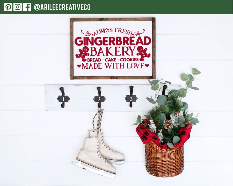 Może przedstawiać: Biała ściana z drewnianym znakiem z napisem "ALWAYS FRESH GINGERBREAD BAKERY" na czerwono. Poniżej znaku znajduje się biały wieszak z trzema haczykami. Para łyżew wisi na środkowym haczyku. Kosz z zielenią znajduje się po prawej stronie.