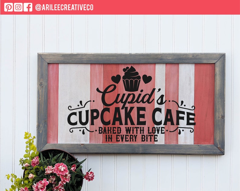 Op de afbeelding: Een houten bord met een rood-wit-grijze gestreepte achtergrond. Het bord luidt "Cupid's Cupcake Cafe - Baked with love in every bite".