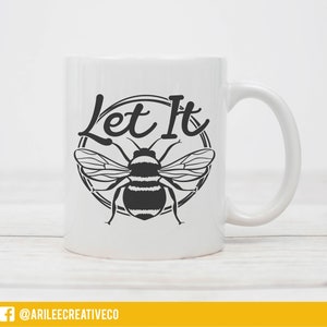 Peut inclure: Une tasse en c&eacute;ramique blanche avec un motif noir et blanc d'une abeille et le texte "Let It" dans un cercle.