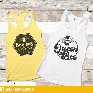Peut inclure: Deux d&eacute;bardeurs blancs avec des motifs d'abeilles noires. Le d&eacute;bardeur de gauche dit "Bee my Honey" et le d&eacute;bardeur de droite dit "Queen Bee".
