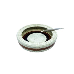 Pode incluir: Um cinzeiro de cerâmica branca com listras marrons e pretas. Um cigarro parcialmente fumado está descansando no cinzeiro.