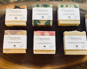 May include: Eight bars of handmade soap with various scents and colors. The soaps are arranged on a wooden cutting board. The labels on the soaps read "Cedarwood Rosemary & Patchouli", "Cedarwood & Bergamot", "Sandalwood Bergamot", "Palma, Fig & Orange", "Orange Rosemary Patchouli", "Lavender Lemongrass", "Lavender Peppermint", and "Lavender Honey & Oatmeal".