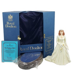 May include: A Royal Doulton figurine of The Duchess of York in a wedding dress, with a bouquet. The figurine is displayed with its original box, a blue information card, and a base. The box is navy blue with gold lettering.