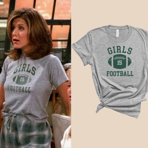 May include: A gray t-shirt with a green football graphic and the text "Girls 15 Football".