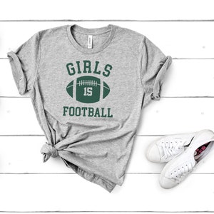 May include: Gray t-shirt with the text "GIRLS FOOTBALL" and a green football with the number 15 on it.