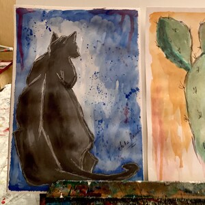 May include: A watercolor painting of a black cat sitting on a blue background with white splatters. The cat is facing away from the viewer. The artist's signature, "shura pachidi", is in the bottom right corner.