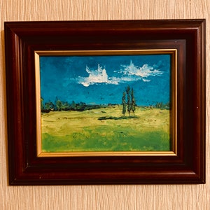 May include: A framed painting of a landscape with a blue sky, white clouds, and green grass. There are three trees in the distance.