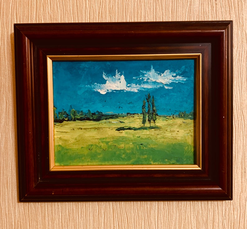 May include: A framed painting of a landscape with a blue sky, white clouds, and green grass. There are three trees in the distance.