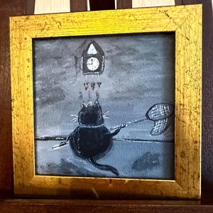 Puede incluir: Pintura enmarcada que representa un gato negro con una red de mariposas, apuntando a un reloj. La obra de arte est&aacute; sobre un fondo gris con un marco dorado. El reloj est&aacute; encima del gato.