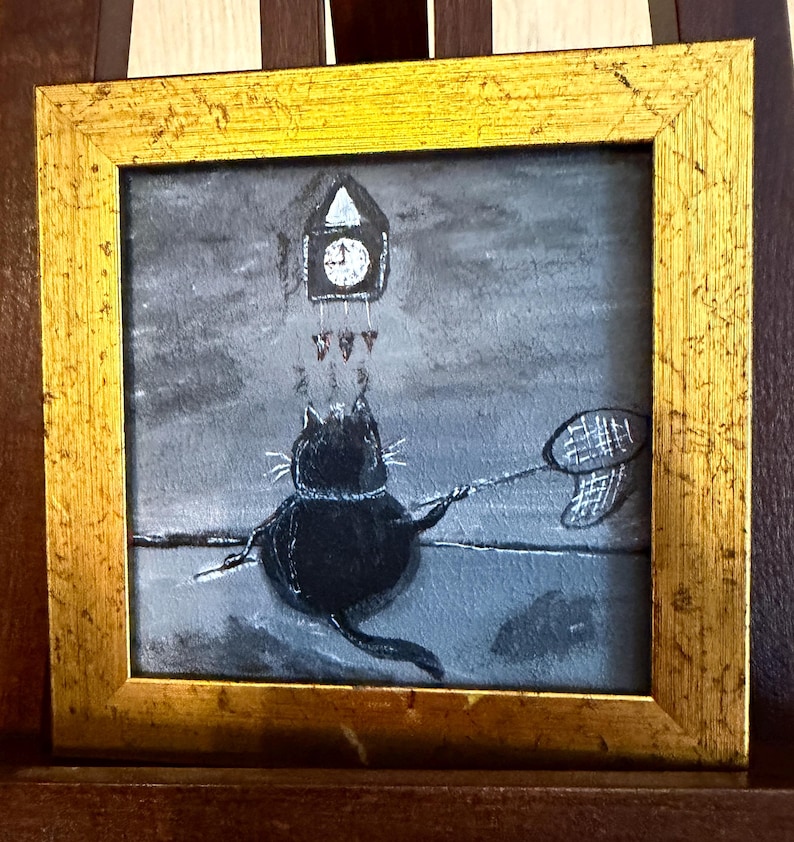 Puede incluir: Pintura enmarcada que representa un gato negro con una red de mariposas, apuntando a un reloj. La obra de arte est&aacute; sobre un fondo gris con un marco dorado. El reloj est&aacute; encima del gato.