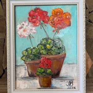 May include: An oil painting of geraniums in terracotta pots, set against a light blue background. The flowers are in shades of red, orange, and white, with green foliage. The painting is in a white frame with gold accents. Signed "JB 2016".