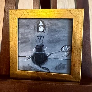Puede incluir: Pintura enmarcada que representa un gato negro que intenta atrapar un reloj con una red de mariposas. La obra de arte est&aacute; en escala de grises con un marco dorado. El gato es el foco, con el reloj y la red.