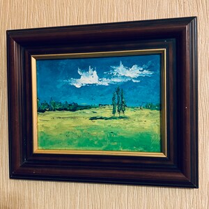May include: A framed oil painting depicting a landscape with a blue sky, white clouds, and three green trees in a field. The painting is in a dark brown frame.