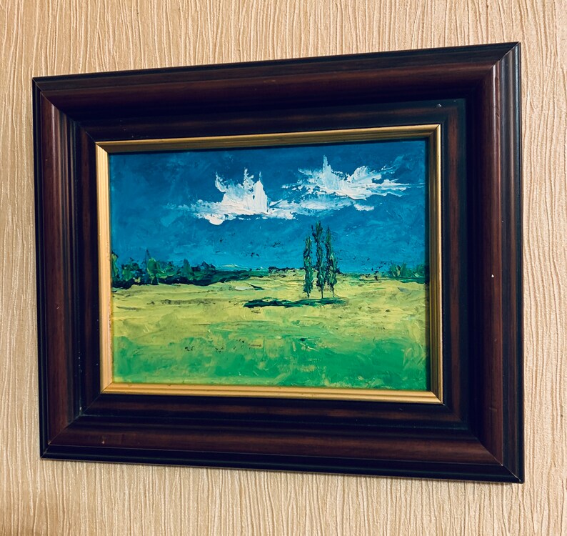 May include: A framed oil painting depicting a landscape with a blue sky, white clouds, and three green trees in a field. The painting is in a dark brown frame.