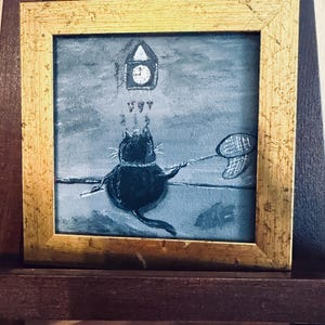 Puede incluir: Pintura enmarcada cuadrada con un marco dorado. La obra de arte representa un gato negro con una red de mariposas, mirando un reloj. El fondo es azul y gris apagado. La pintura se exhibe en un caballete de madera.