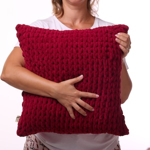 May include: A close-up of a red knitted throw pillow. The pillow is soft and fluffy, and it has a chunky knit texture.