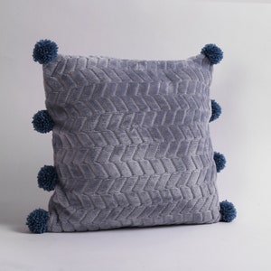 May include: A gray throw pillow with a textured chevron pattern and blue pom-poms around the edges.