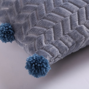 May include: A gray throw pillow with a chevron pattern and blue pom-poms on the corners.