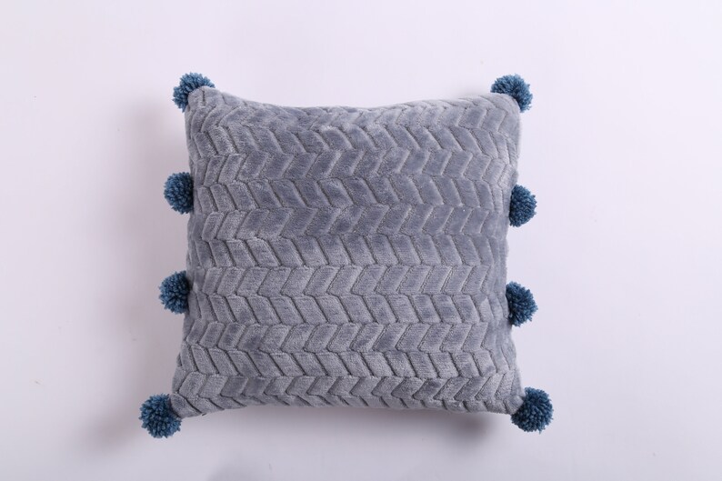May include: Gray throw pillow with a textured chevron pattern and blue pom-poms around the edges.