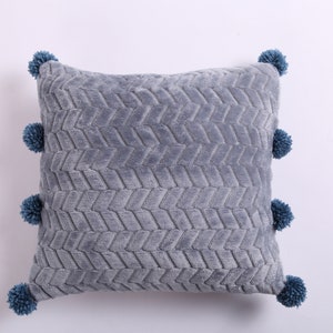 May include: A gray throw pillow with a textured chevron pattern and blue pom-poms around the edges.
