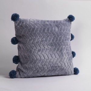 May include: A gray throw pillow with a textured chevron pattern and blue pom-poms around the edges.